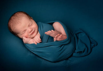 A newborn baby lying on turquoise blanket and swaddle. The background is a turquoise colour.