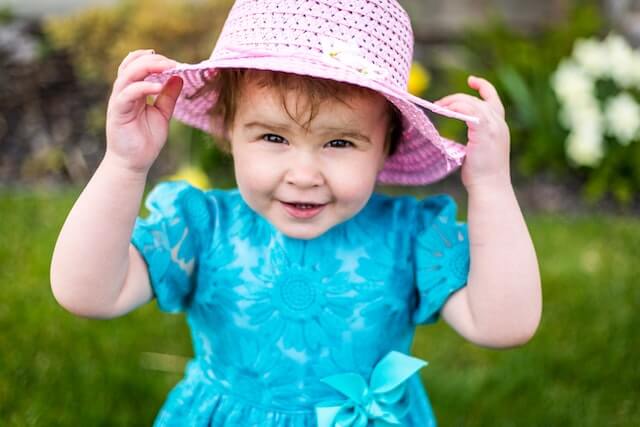 Smiling baby girl wearing a turquois colour dress and a pink hat from OleOle