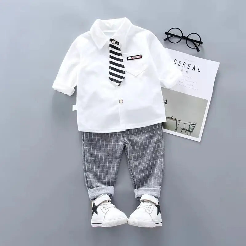 Children's outfit with white shirt, striped tie, plaid pants, and sneakers on a gray background.