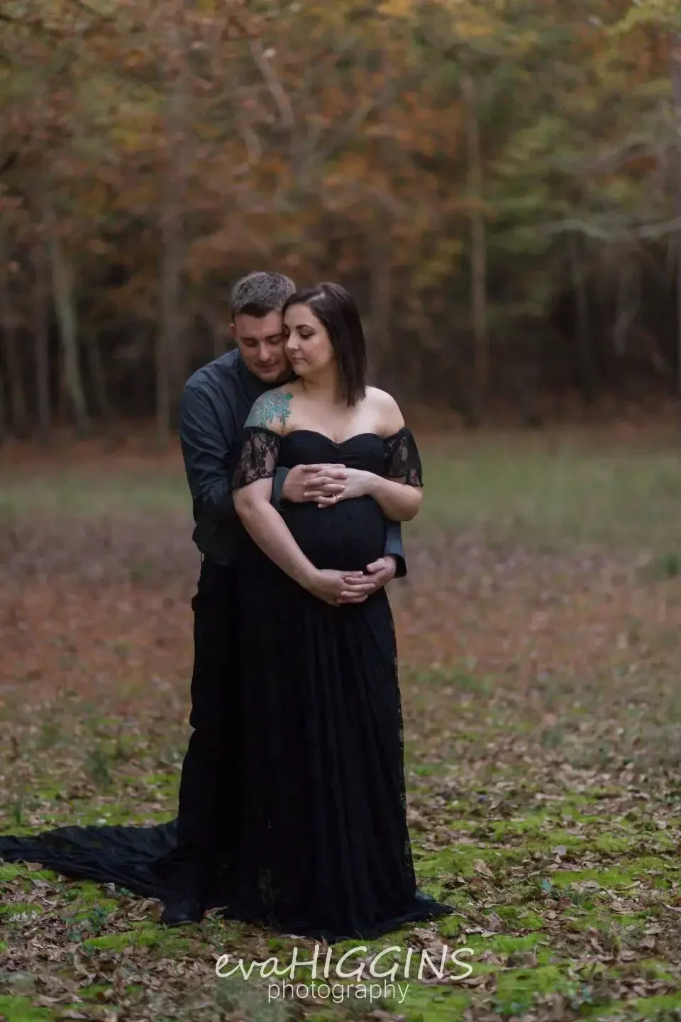 Pregnant woman in a black dress standing with a man in a forest setting.