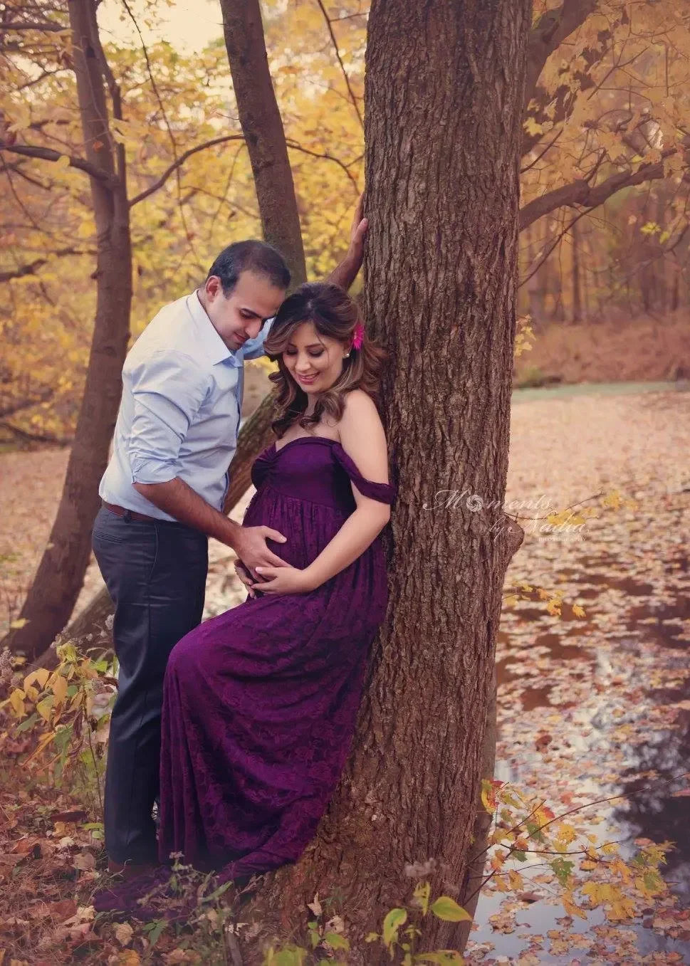 Pregnant woman in a purple dress standing next to a man in an autumn forest.