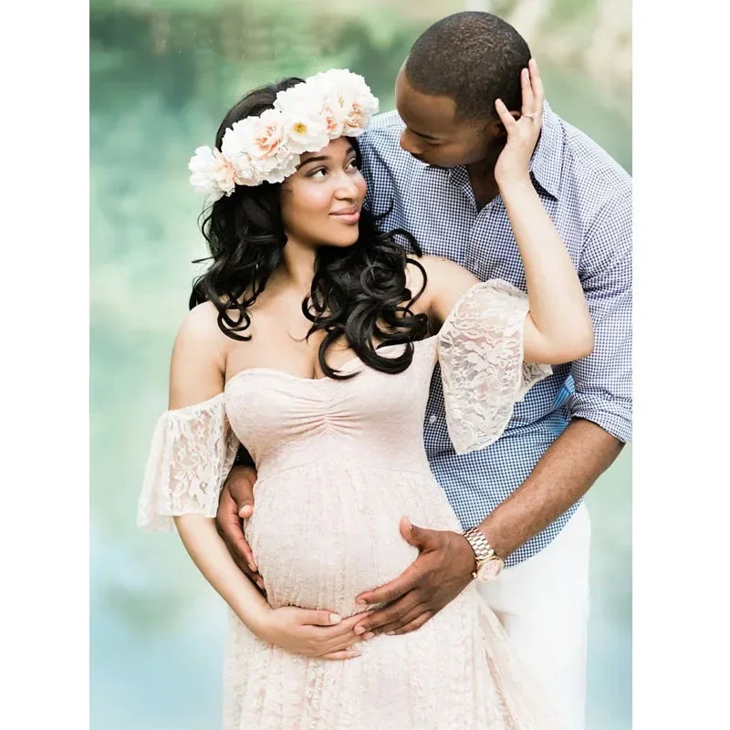 Pregnant woman in a white lace dress with a man embracing her outdoors.