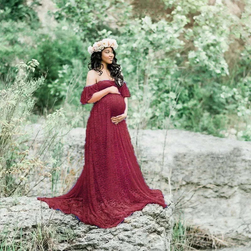 Pregnant woman in a red lace dress standing in a natural setting with greenery.