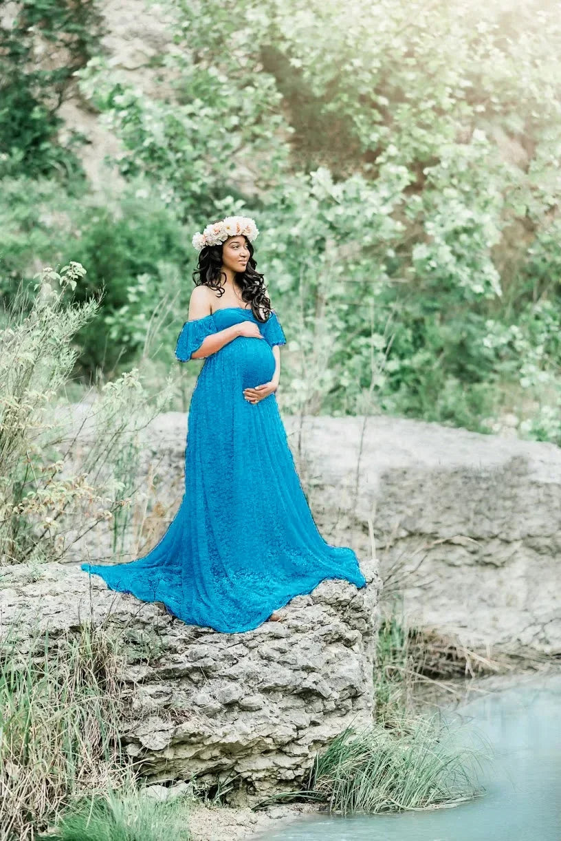Woman in a blue gown standing on rocks by a stream with greenery in the background
