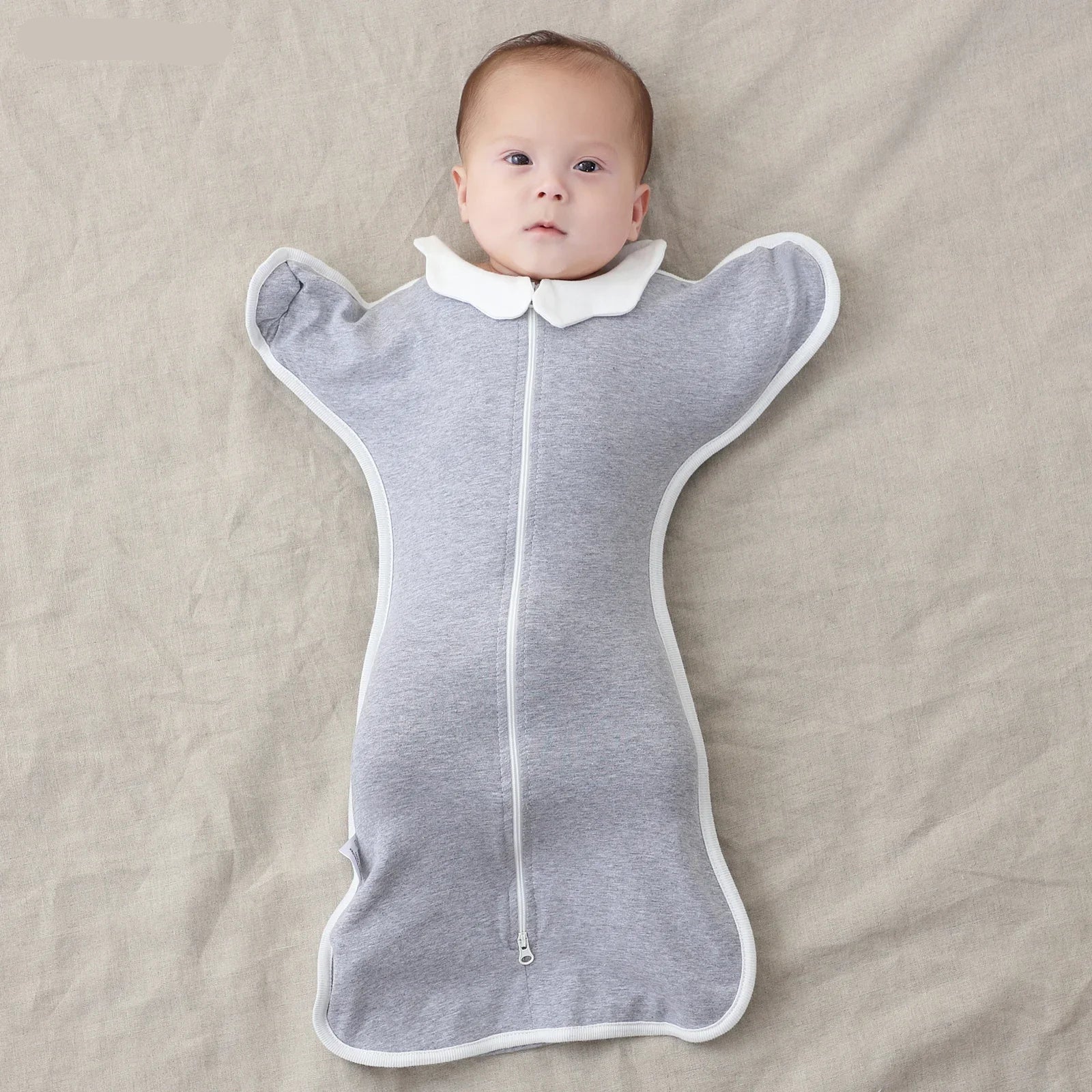 Baby in a gray sleeping bag with a collar on a beige blanket, branded 'Insular'.