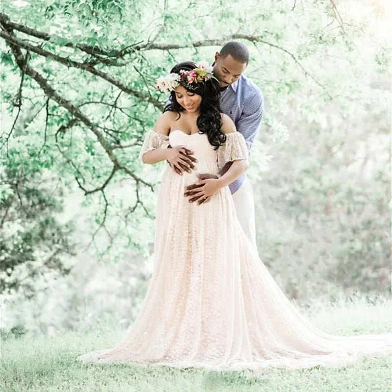 Pregnant woman in a flowing dress standing outdoors with a man, surrounded by nature.